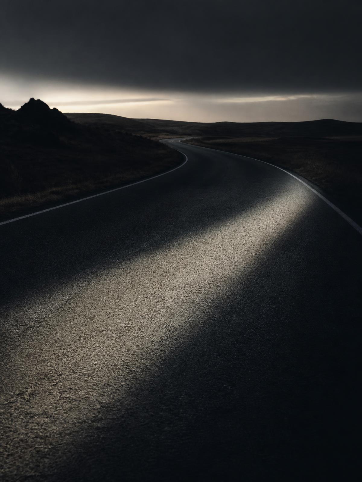 Empty road curving through open landscape at dusk, cut by a band of light